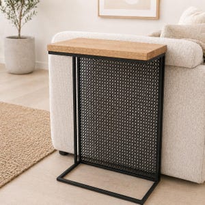 May include: A contemporary side table with a rectangular, light-coloured wooden top and a black metal frame. The table features a decorative, black mesh panel and is designed to slide alongside a sofa. The table is approximately 61 cm long.