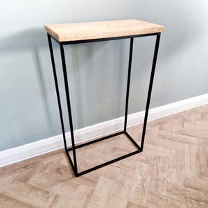 May include: A black metal console table with a rectangular wooden top. The table has a simple, modern design and is ideal for a hallway or entryway.