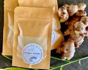 May include: Four small brown paper pouches with a white label that reads "Kalalea View Farm Ginger Powder".  Fresh ginger root is visible in the background.