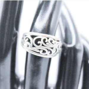 May include: A silver ring with a delicate, intricate design. The ring is made of a thin band with a filigree pattern that resembles leaves or vines.