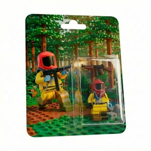 Könnte beinhalten: Verpacktes Spielzeugset mit zwei Figuren in gelben Schutzanzügen und roten Helmen. Eine Figur hält ein schwarzes Gewehr, die andere ein braunes Gewehr. Der Hintergrund zeigt eine Waldszene.