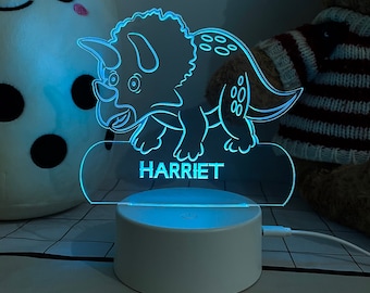 May include: A blue light-up nightlight shaped like a triceratops dinosaur with the name "HARRIET" printed on the base.