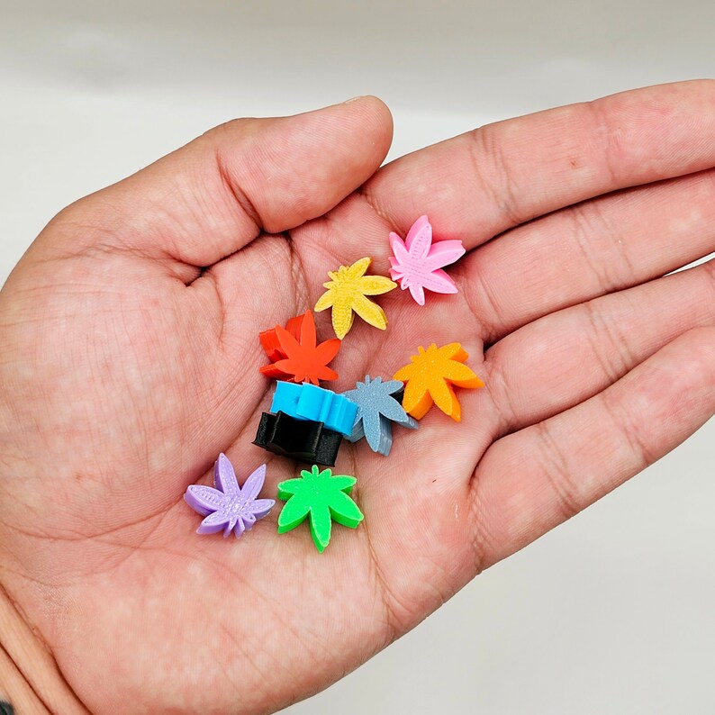 May include: A collection of colorful, small, plastic leaf-shaped charms in various colors, including purple, orange, yellow, blue, green, and pink.