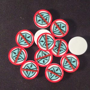 May include: A collection of game tokens with a red border, a white background, and a blue symbol crossed out with a red line. Two white tokens are also present. The tokens are likely for a board game.