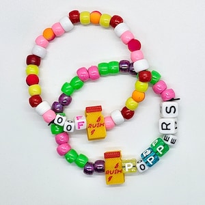 May include: Two colorful beaded bracelets with letter beads spelling out "OFF RUSH" and "POPPERS". The beads are in various colors, including red, orange, yellow, green, blue, pink, and white. The bracelets are made of plastic.