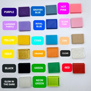 May include: A collection of 16 small plastic squares in various colors, including purple, blue, pink, yellow, cyan, tan, gold, orange, clear, black, green, red, and white. The squares are labeled with the color names, and some have additional text, such as "Glow in the Dark" and "Neon Green".