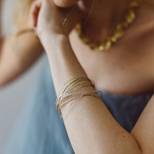 Puede incluir: Primer plano de un brazo de mujer con una pila de brazaletes finos de oro y plata. Los brazaletes están superpuestos y crean un look delicado y elegante.