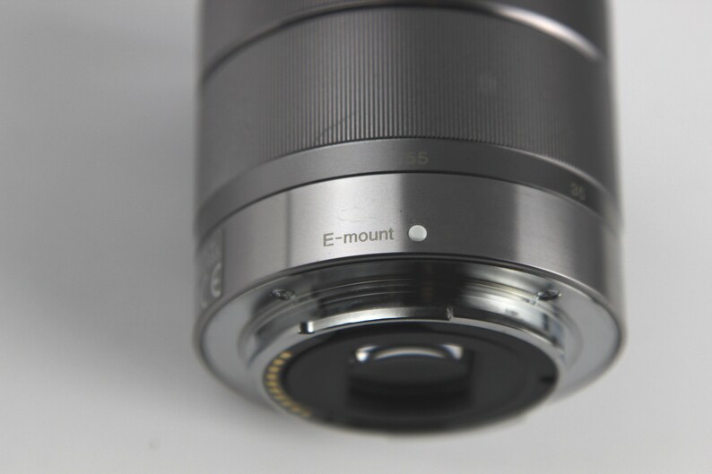 Puede incluir: Un objetivo de c&aacute;mara plateado con una tapa de lente negra y el texto "E-mount" impreso en el lateral.