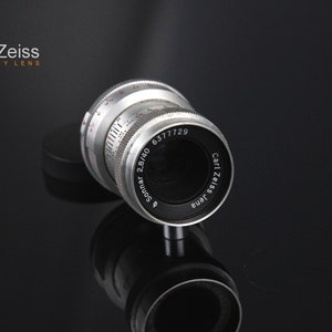 May include: A silver camera lens with the text "Sonnar 2.8/40 6377729 Carl Zeiss Jena" printed on the side.