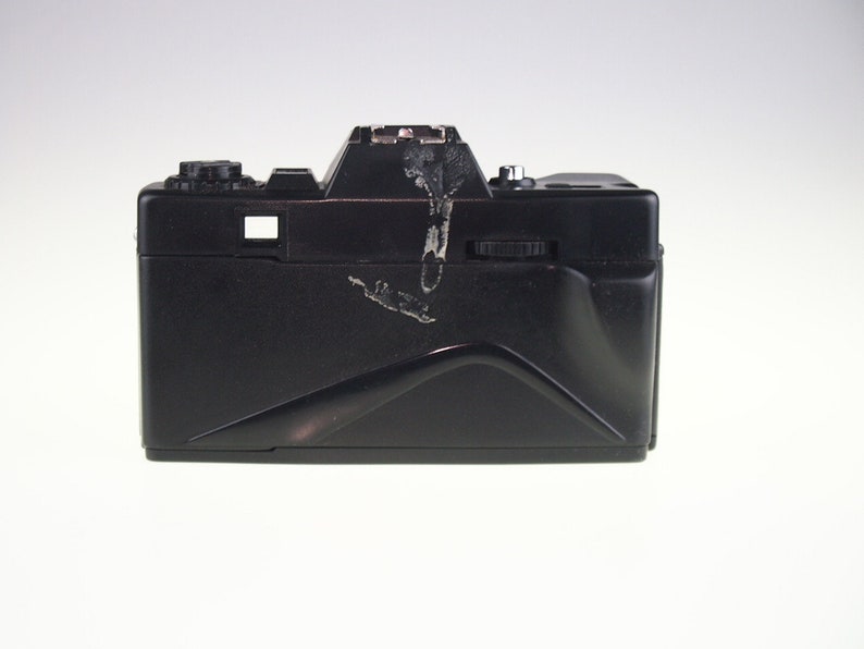 May include: A black 35mm film camera with a built-in flash. The camera has a few scratches and scuffs on the surface.