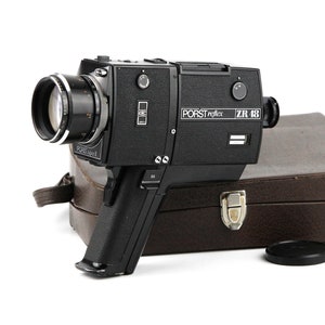 May include: A black and silver 8mm film camera with a lens and a carrying case. The camera has the text "PORST reflex ZR 48" on the side.