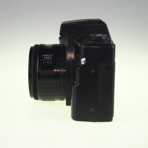 May include: A black 35mm film camera with a focus free lens. The lens has the text "FOCUS FREE 1:6.3" printed on it.