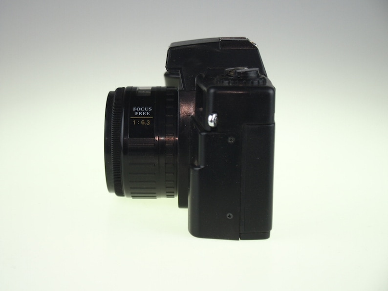 May include: A black 35mm film camera with a focus free lens. The lens has the text "FOCUS FREE 1:6.3" printed on it.
