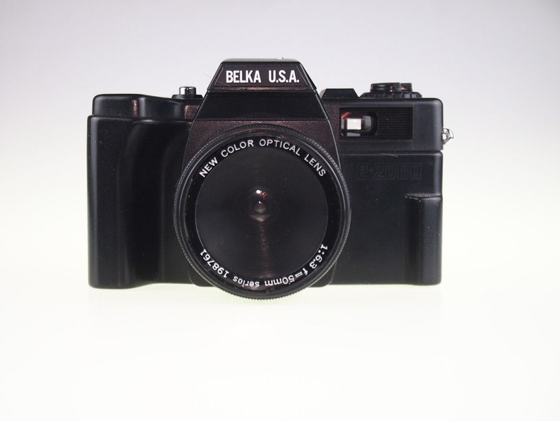 May include: A black Belka U.S.A. 1-2000 camera with a New Color Optical Lens. The lens is labeled 1:6.3 f-50mm series 198761.