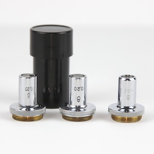 May include: Three silver microscope objective lenses with black markings, labeled "0.20", "0.40", and "0.60", in a black plastic storage case.
