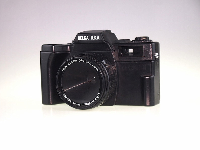 May include: A black Belka U.S.A. 35mm film camera with a New Color Optical lens. The lens has the text "1:6.3 f-50mm series 198761" printed on it.