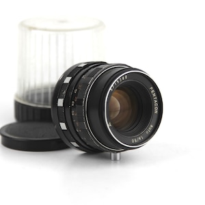 May include: A black Pentacon 18/50 mm lens with a silver ring and markings. The lens is in focus and the aperture is open.
