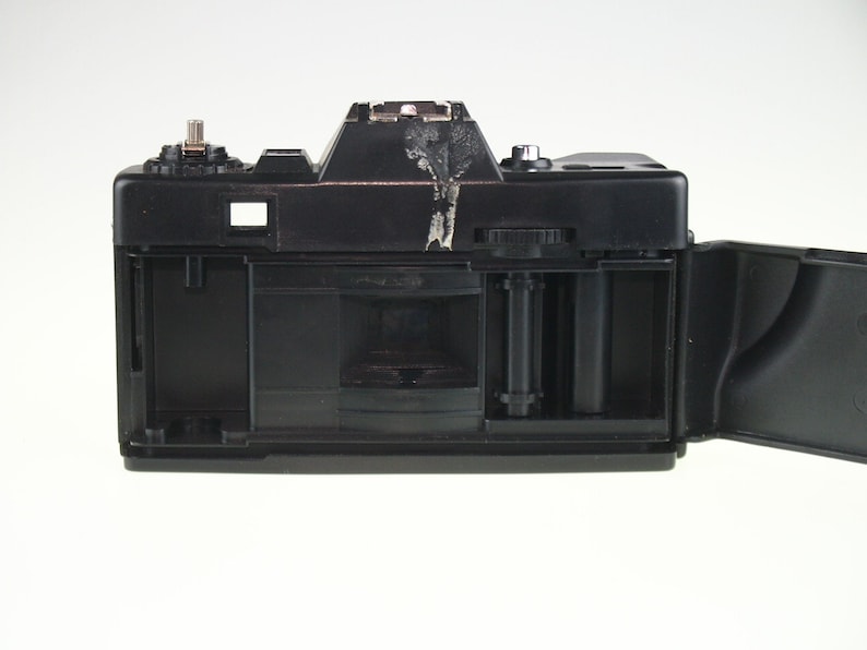 May include: A black 35mm film camera with the back open, revealing the film compartment and a roll of film.