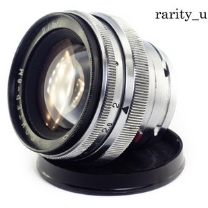 May include: A silver and black camera lens with the text "Jupiter-8 M" and "2/50" printed on the side. The lens has a silver aperture ring with markings from 2.8 to 22.