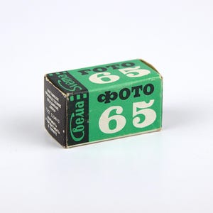 Peut inclure: Une boîte de pellicule "Фото 65" de la marque "Smena", de couleur verte et noire.