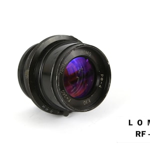 Op de afbeelding: Zwarte LOMO RF-4 cameralens met een paars en blauw reflecterend interieur. De lens heeft een reeks ringen en markeringen, waaronder "F=360" en "1:10". De tekst "LOMO RF-4" is rechtsonder in het wit gedrukt.