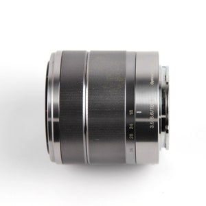 Puede incluir: Un objetivo de c&aacute;mara plateado con un anillo negro alrededor del frente. El objetivo tiene marcas para 18, 24, 28 y 35 mm. El texto "3.5-5.6/18-55" est&aacute; impreso en el lateral del objetivo.