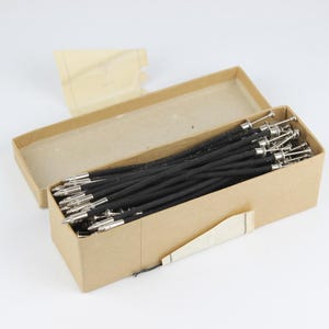 May include: A cardboard box filled with black elastic hair ties with metal ends. The box is open and the hair ties are visible.