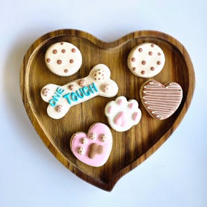 May include: A heart-shaped wooden tray with six decorated cookies. The cookies are decorated with paw prints, hearts, and the words "One Touch".