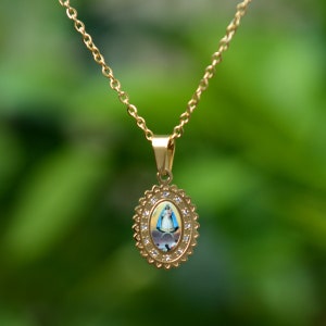 May include: A gold chain necklace with a pendant featuring a religious image of the Virgin Mary in an oval frame with clear rhinestones.