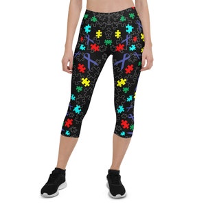 Puede incluir: Leggins negros con un patrón de piezas de rompecabezas y cintas de colores. El patrón es una representación de la concienciación sobre el autismo.