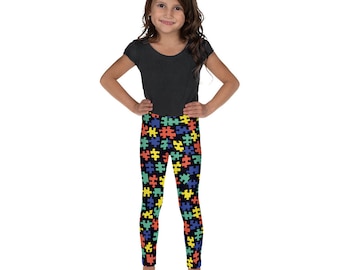 May include: A young girl wearing black leggings with a colorful puzzle piece pattern. The leggings are made of a soft, stretchy material and are perfect for everyday wear.