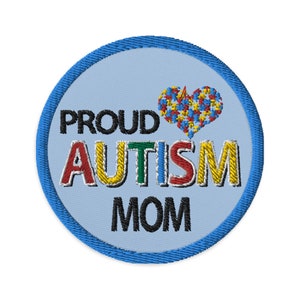 Könnte beinhalten: Ein runder gestickter Aufnäher in Blau und Weiß mit dem Text "PROUD AUTISM MOM" und einem Herz aus Puzzle-Teilen in Rot, Gelb, Blau und Grün.