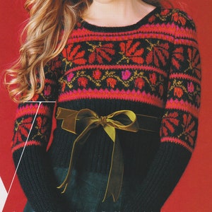 Peut inclure: Un pull noir avec un motif géométrique coloré et un ruban de velours vert noué autour de la taille. Le pull a un col rond et des manches longues.