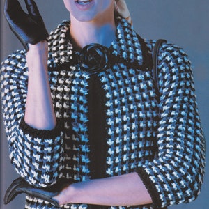 May include: A black and white houndstooth patterned jacket with a black rose brooch. The jacket has a black trim and is paired with black sunglasses and gloves. A patterned scarf and headband complete the look, creating a vintage fashion aesthetic.