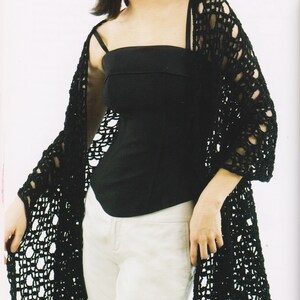 May include: A black, open-weave crochet cardigan. The long-sleeved garment is worn over a black top and white pants. The crochet pattern features large, open spaces, creating a delicate, airy look. The cardigan's edges have a scalloped trim.