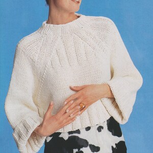 May include: A white knitted sweater with a high neckline and a cable knit pattern. The sweater has long sleeves and a relaxed fit.