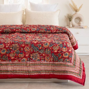 Könnte beinhalten: Eine rote Blumenbettwäsche mit blauem und braunem Rand. Die Bettwäsche liegt auf einem Bett mit weißen Kissen.