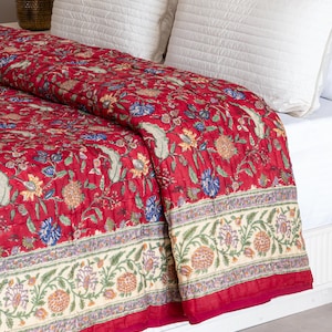 May include: Red floral quilt with a white border and a floral pattern. The quilt is folded on a white bed with white pillows.