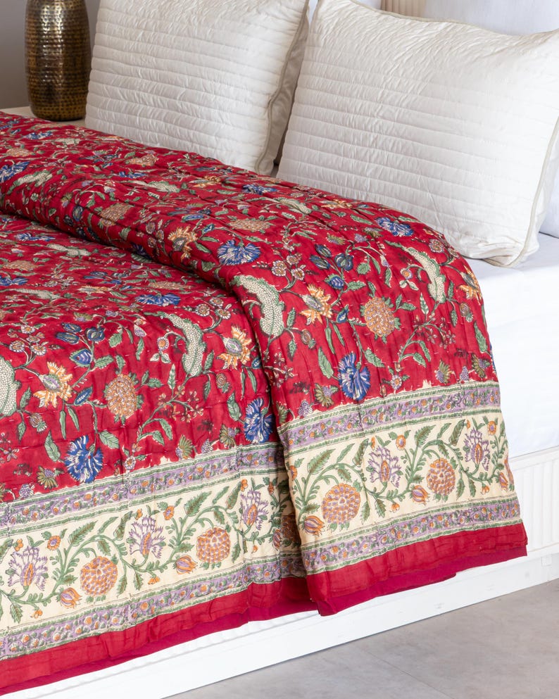 May include: Red floral quilt with a white border and a floral pattern. The quilt is folded on a white bed with white pillows.