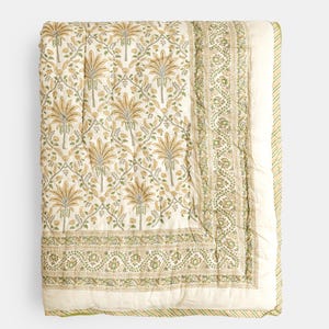 May include: A folded, cream-colored quilt with a repeating pattern of stylized palm trees in shades of gold and green. The border features a detailed floral design in green and cream, with a striped edge.
