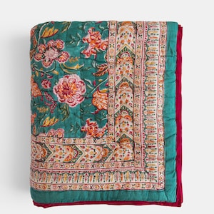 Op de afbeelding: Een opgevouwen teal quilt met een bloemenpatroon in tinten oranje, roze en geel. De quilt heeft een decoratieve rand en een dieprode rand. De quilt is gemaakt van een zacht, gewatteerd materiaal.