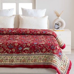 May include: A red floral quilt with a cream border and a floral pattern. The quilt is on a white bed with white pillows.