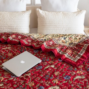 May include: A red floral quilt with a laptop computer on top. The quilt has a white border and a yellow and white floral pattern on the reverse side.