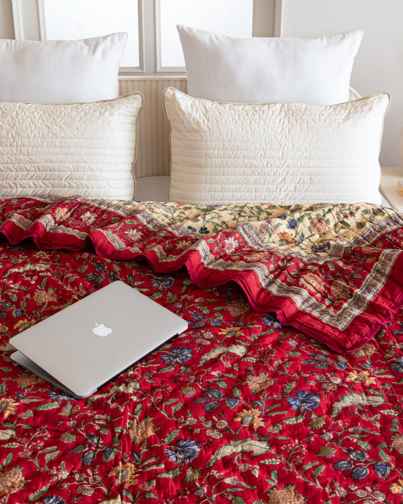 May include: A red floral quilt with a laptop computer on top. The quilt has a white border and a yellow and white floral pattern on the reverse side.