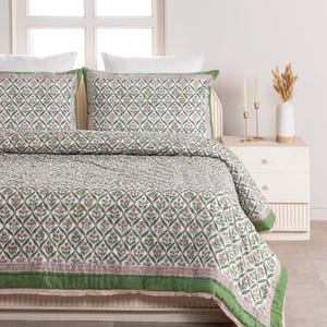 May include: A bed with a floral patterned quilt and matching pillowcases. The quilt features a repeating pattern of green leaves and pink flowers on a white background, with a green border. The pillowcases have a similar design.