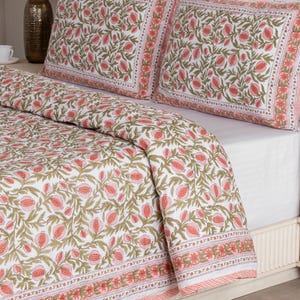 May include: White bedding set with a floral pattern in shades of pink and green. The set includes a comforter and two pillowcases. The floral design is repeated across the entire set, with a border of pink and white stripes.