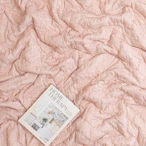 May include: A quilted, peach-colored blanket with vertical white stripes. The blanket is rumpled, creating a textured appearance. A book titled "HOME THERAPY" is lying on top of the blanket.