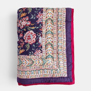 K&ouml;nnte beinhalten: Eine lila und wei&szlig;e, floral gemusterte Steppdecke mit rotem Rand. Die Steppdecke ist aus Baumwolle und handgen&auml;ht.