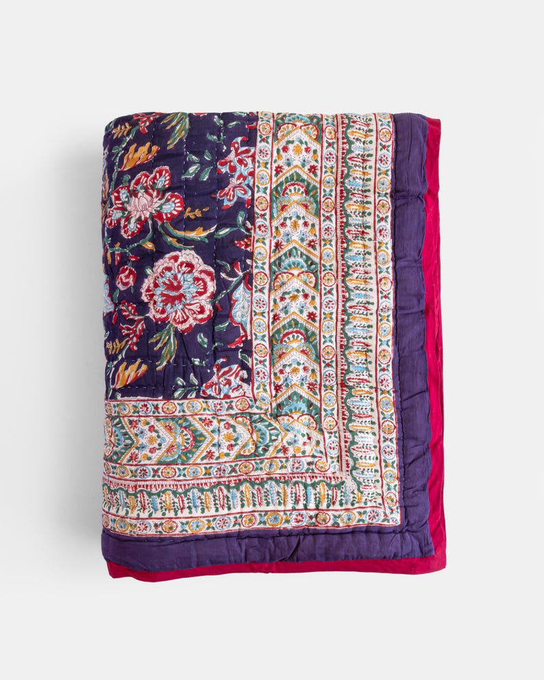 K&ouml;nnte beinhalten: Eine lila und wei&szlig;e, floral gemusterte Steppdecke mit rotem Rand. Die Steppdecke ist aus Baumwolle und handgen&auml;ht.