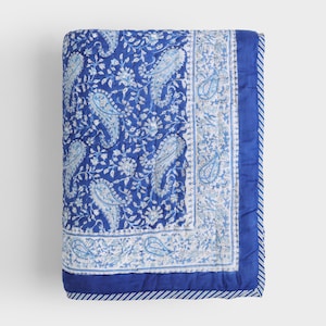 May include: A folded blue quilt with a paisley pattern in white and light blue. The quilt has a solid blue border with a striped edge. The overall design is a floral and paisley print.